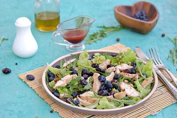 Light salad with arugula, lettuce, grilled chicken and honeysuckle on a brown plate on a turquoise background. Healthy food, diet. Selective focus