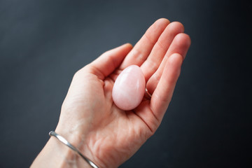woman holding in hand a vaginal (yoni) egg. Rose quartz crystal jade egg. Copy space