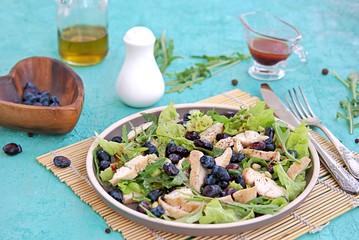 Light salad with arugula, lettuce, grilled chicken and honeysuckle on a brown plate on a turquoise background. Healthy food, diet. Selective focus