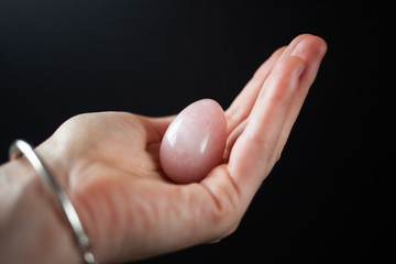 woman holding in hand a vaginal (yoni) egg. Rose quartz crystal jade egg. Copy space