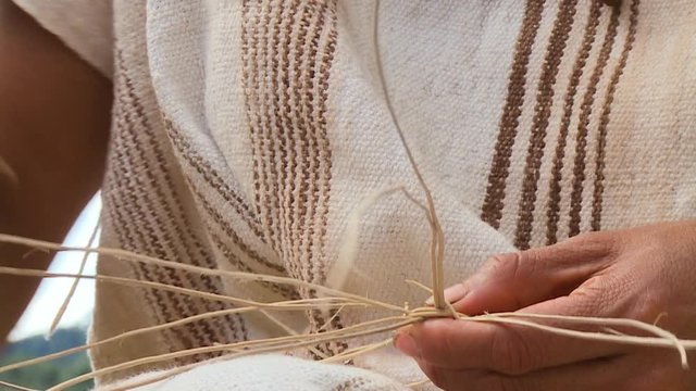 Extreme close-up low-angle still shot of a man wearing a traditional shirt beginning to weave a traditional men's hat using local straws, Cusco, Peru