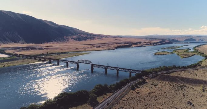 A drone flyby shot of Beverly Bridge in front of its mountainous landscape, in Washington, USA, on a sunny day. The wide river sparkles under the sunlight.