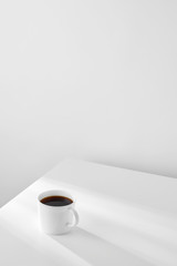 White coffee cup on the table against white wall with copy space. Morning light entering from the window. Minimalism. 