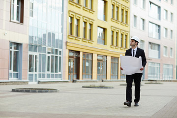 Full length portrait of handsome Middle-Eastern businessman wearing hardhat walking towards camera at construction site, copy space