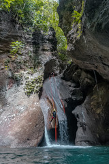 Adventure seeker rappels down a beautiful waterfalls with a clear turquoise green water below.