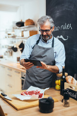 middle aged man browsing online recipes on tablet in his home kitchen