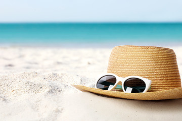 Hat and sunglasses on sand near sea, space for text. Stylish beach accessories