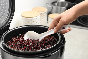 Woman taking brown rice from multi cooker with spoon in kitchen, closeup