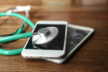Smartphones and stethoscope on wooden table, closeup with space for text. Repairing service
