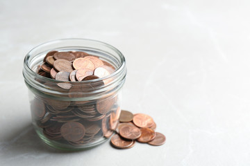 Glass jar and coins on light background. Space for text