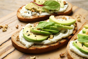 Delicious bruschettas with avocado served on wooden board, closeup