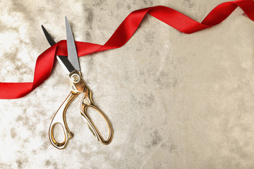 Stylish scissors and red ribbon on color background, flat lay with space for text. Ceremonial tape...