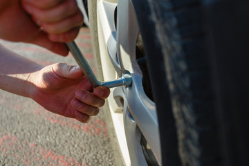 Obraz premium Close-up hands with cylinder wrench unscrew damaged wheel of car. Man changes flat wheel after car breaks down. Wheel balancing, repair and replacement car tires on wheels. Tire installation concept