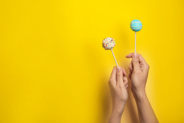 Woman holding bright delicious cake pops on color background, closeup. Space for text