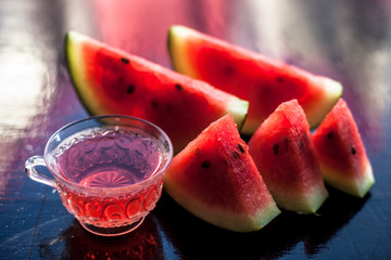 Mouth-watering watermelon tea in a transparent glass cup on wooden surface with watermelon pieces in triangle shape.