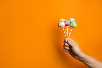 Woman holding bright delicious cake pops on color background, closeup. Space for text
