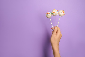 Woman holding bright delicious cake pops on color background, closeup. Space for text