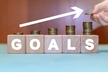 Goal finance business concept. Hand is putting coin on growing stacks of coins on wooden cubes. Financial Goals Invest.