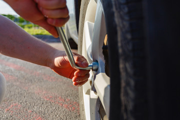 Close-up hands with cylinder wrench unscrew damaged wheel of car. Man changes flat wheel after car breaks down. Wheel balancing, repair and replacement car tires on wheels. Tire installation concept