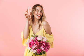 Beautiful amazing young blonde woman posing isolated over pink wall background holding flowers...