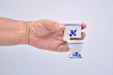 Mano sujetando un inodoro de miniatura sobre fondo blanco
