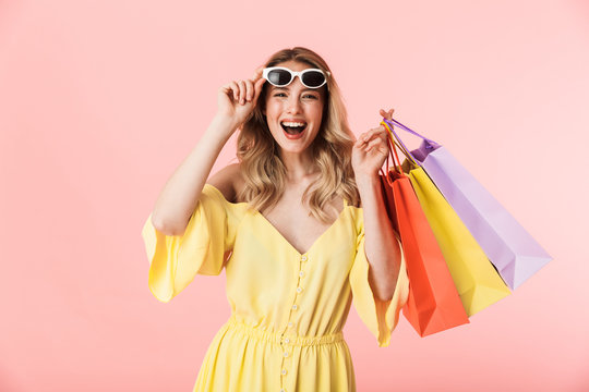 Beautiful shocked young blonde woman posing isolated over pink wall background holding shopping bags.