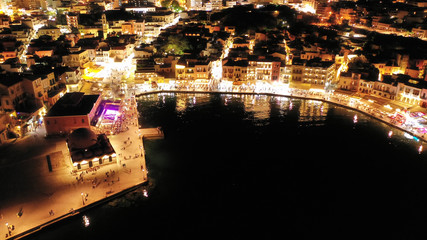 Aerial drone night shot of iconic and picturesque illuminated Venetian old port of Chania with famous landmark lighthouse and shops - restaurants serving Cretan traditional food, Crete island, Greece