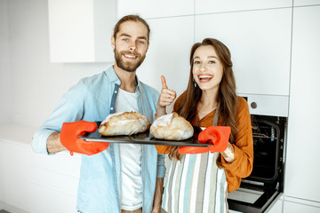Portrait of a young beautiful couple holding tray with fresh baked breads in the modern bright...