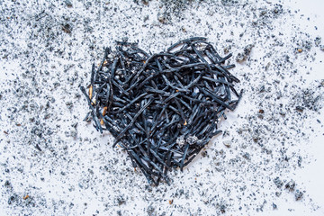 Heart symbol made of burned-down matches close-up with ashes around. The concept of the complexity of love relationships, unhappy love.