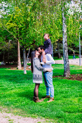 Fototapeta premium Family mom, dad and daughter sits at the daddy on the shoulders, and parents kiss on the park at daylight
