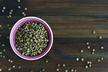 Dried green peppercorns in a violet bowl. Dark wooden table, high resolution