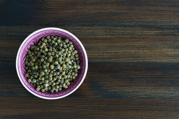 Dried green peppercorns in a violet bowl. Dark wooden table, high resolution, negative space