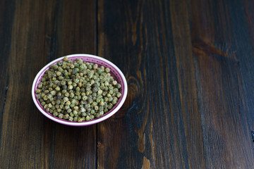 Dried green peppercorns in a violet bowl. Dark wooden table, high resolution, negative space