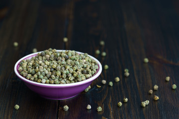 Dried green peppercorns in a violet bowl. Dark wooden table, high resolution, negative space