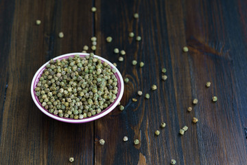 Dried green peppercorns in a violet bowl. Dark wooden table, high resolution