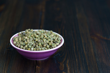Dried green peppercorns in a violet bowl. Dark wooden table, high resolution, negative space