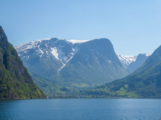 Obraz premium A view on the Songefjorden (King of the Fjords) from the water level. It is the deepest fjord in Norway. Tall, lush green mountains surrounding the fjord. Calm surface of the water. Clear blue sky.