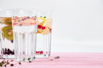 Variety of  Detox infused water with  kiwi, apple, lavender, ginger, lemon, mint on pink background. Refreshing summer homemade cocktail. Diet. Healthy drink. Copy space.