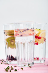 Variety of  Detox infused water with  kiwi, apple, lavender, ginger, lemon, mint on pink background. Refreshing summer homemade cocktail. Diet. Healthy drink..