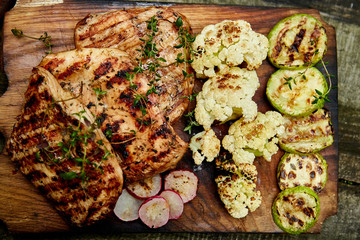 Grilled turkey meat. Steak turkey grill on wooden cutting board with a variety of grilled vegetables on  rustic background  Top view. Flat lay. Copy space..