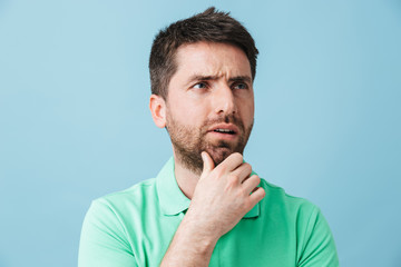 Thinking serious young handsome bearded man posing isolated over blue wall background.