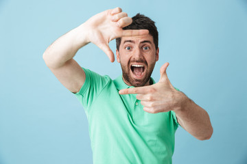 Fototapeta na wymiar Happy young handsome bearded man posing isolated over blue wall background make photo frame gesture.