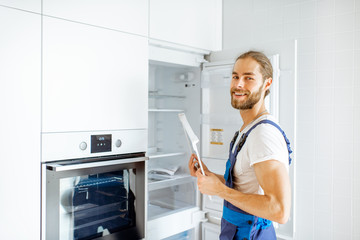 Portrait of a handsome workman installing new refrigerator in the modern kitchen at home