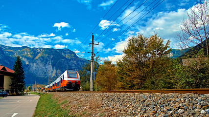 Red blue train in motion in Austrian alps mountains. High speed mountain train arrives at Hallstatt Obertraun train station in mountains. Location: resort village Hallstatt, Salzkammergut, Austria
