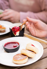 Breakfast with friends in a summer cafe in the open air. On the table are dessert fried cottage cheese pancakes with red jam, orange juice and black coffee. Hands in the frame with golden cutlery.