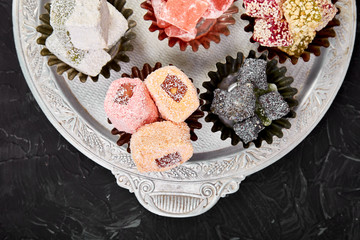 Set of various Turkish delight in traditional silver bowl on metal tray black background.Middle Eastern dessert. Top view. Flat lay