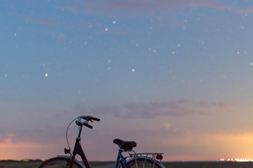 Night photography bicycle at night on the countryside with the stars and city lights in the background