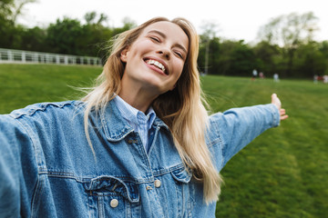 Amazing excited happy young woman posing outdoors in park take a selfie by camera.