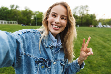 Amazing excited happy young woman posing outdoors in park take a selfie by camera.