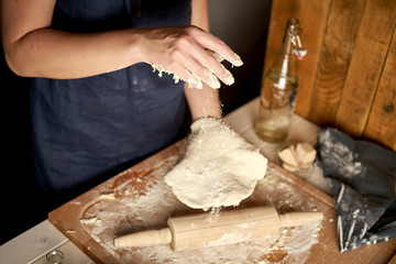 Woman prepares dough on pastry board with flour and rolling pin on wooden table